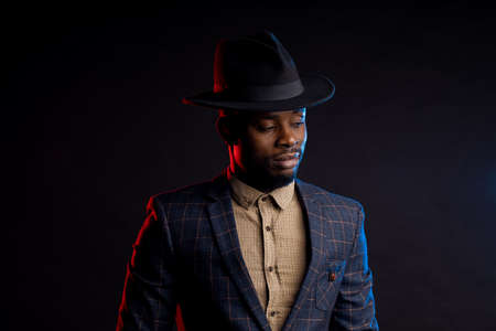 Stylish African man in hat looking down, copy space, on dark backgroundの写真素材
