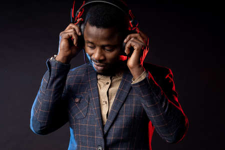 Closeup  young  man listening music in headphones, enjoying with closed eyes, standing in dark. Portrait of stylish DJ with headset isolated over black background.の写真素材