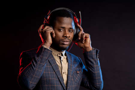 man listening music with headphones in dark background. Portrait of stylish DJ with headset, wearing checked suit, isolated on black backgroundの写真素材