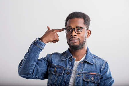Shot of serious tired attractive black man shooting in temple with index finger, demonstrating suicide gesture, pretending killing himself wearing denim jacket, glasses isolated over white background.の写真素材