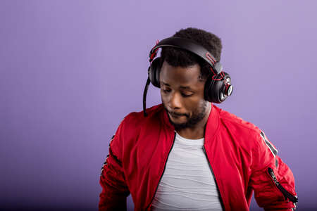 Studio portrait of handsome young black man in headphones, enjoying listening to music and dancing on lilac background. Professional african american DJ in headphones. Close up.の写真素材