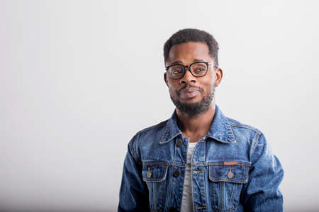 Portrait of good looking confident African American male with small beard wearing casual tshirt and denim jacket posing against gray studio background with serious expression. Copy space.の写真素材