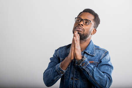 Closeup of young black man praying with hands clasped together, asking the God for good luck, success, health, looking up, isolated gray studio wall. Human emotion, facial expression, belief concept.の写真素材