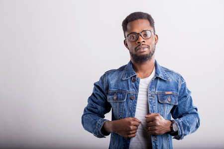 Portrait of good looking confident African American male with small beard wearing casual tshirt and denim jacket posing against gray studio background with serious expression. Copy space.の写真素材