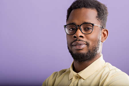 Closeup portrait of handsome unshaven african american man in casual yellow tshirt, eyewear, looking to side posing against lilac studio wall with copy space for your advertisement.の写真素材