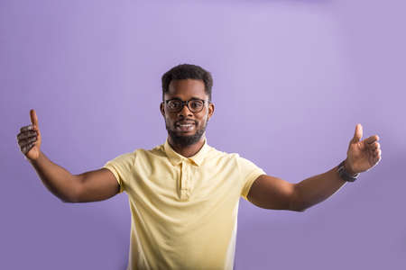 Portrait of friendly happy handsome African American man wearing eyewear, yellow polo tshirt with small beard and short haircut, smiling and pulling hands towards camera wanting to cuddle, hugの写真素材