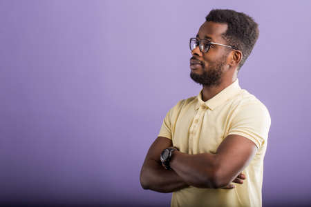 Portrait of confident charismatic young handsome bearded african american male in yellow polo tshirt holding hands crossed on chest looking to side, having interesting conversation. Copy space.の写真素材