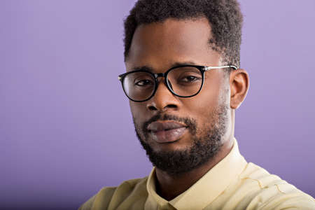 Closeup headshot portrait of handsome serious unshaven african american man wearing casual yellow polo tshirt, eyewear, looking at camera posing against lilac studio wall.の写真素材
