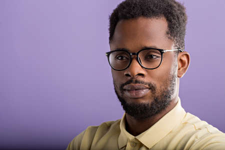 Closeup portrait of handsome unshaven african american man in casual yellow tshirt, eyewear, looking to side posing against lilac studio wall with copy space for your advertisement.の写真素材