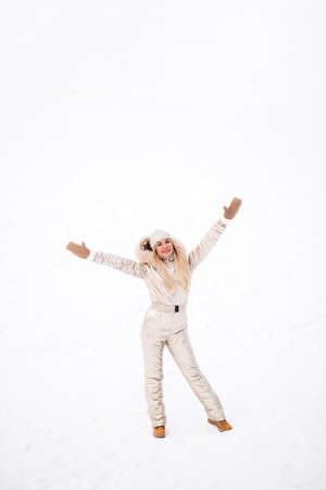 Full-length portrait of blonde european lady wearing stylish golden jumpsuit enjoying free time in winter city, posing with raised hands, smiling to camera. Positive emotions, winter holidays.の写真素材