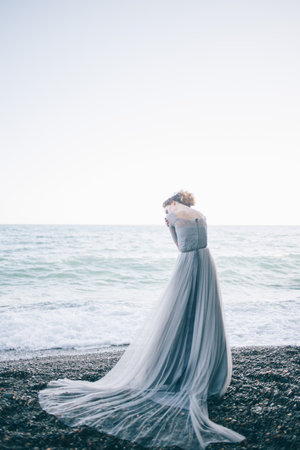 Beautiful girl in a long gray dress with a veil on the beach, waves, summerの写真素材