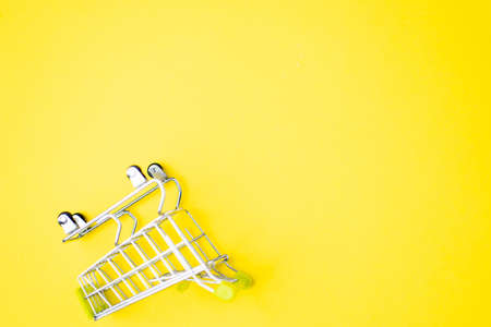 Top view, flat lay shot of shopping cart on bright yellow background. Copy space for text or design. Stainless steel shopping trolley upside down. Minimalist shopping concept.の写真素材