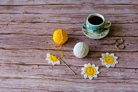 Crocheted daisy, balls of colored yarn, scissors, and a cup of coffee on wooden backgroundの写真素材