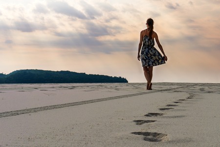 Woman walks on sand beach towards the ocean. Enjoy summer vacation.の写真素材