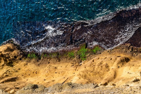 Aerial top view of sea waves hitting rocks on the shore with turquoise sea water. Europe.