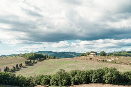 Tuscany, rural sunset landscape. Countryside farm, cypresses trees, green field, sun light and cloud. Volterra, Italy, Europe.の写真素材