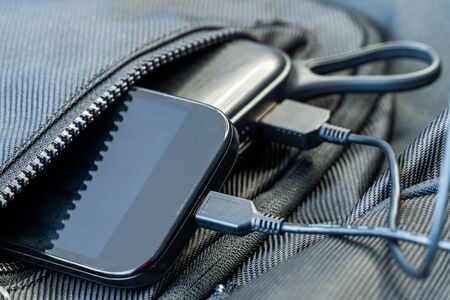 Smartphone charging with black energy bank in backpack, selective focus