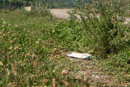 Discarded used medical mask on the side of the road. Human pollution of the environment