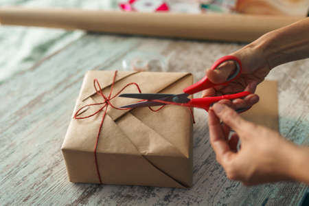 Woman packaging box with kraft wrapping paper and natural twine. Happy holiday present and gifts....