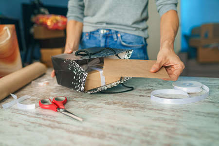 Wrapping holyday gift. Woman decorating stylish gift in craft paper on table in homeの写真素材