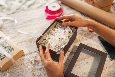 Wrapping holyday gift. Woman Hands decorating stylish gift in craft paper on table in homeの写真素材