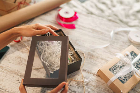Woman wrapping gift boxes at table. Preparing natural eco presents with decor elements.