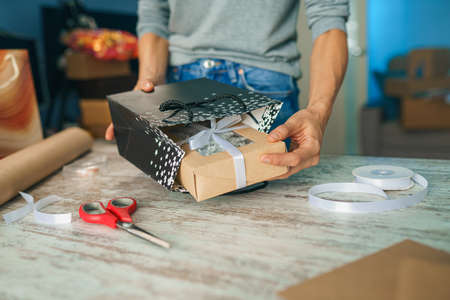Woman wrapping holyday gift, decorating stylish gift in craft paper on table in homeの写真素材