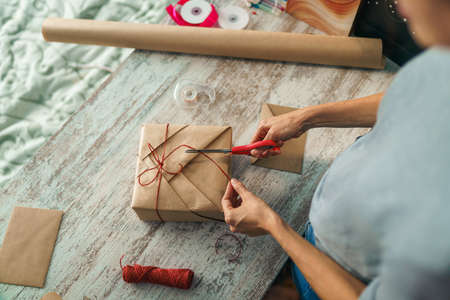 Overhead view of young woman wrapping gift box on table at home