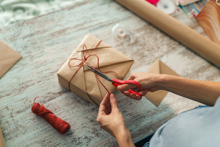 Woman wrapping holyday gift, decorating stylish gift in craft paper on table in home