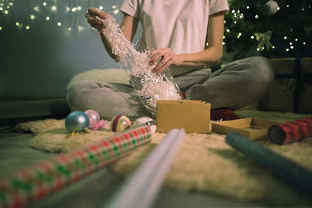 Woman putting kraft shredded paper in packaging box wrapping gift. Happy holiday present and gifts. DIY art craftの写真素材
