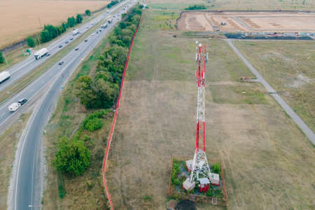 Cell site of telephone tower with 5G base station transceiver by highway with traffic move drive cars. Aerial view of telecommunication antenna mastの写真素材