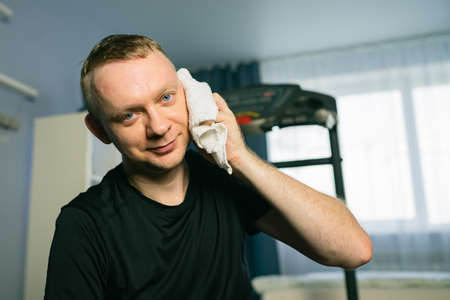 Tired man wiping sweat after exercising on treadmill at home. Cardio Run Workoutの写真素材