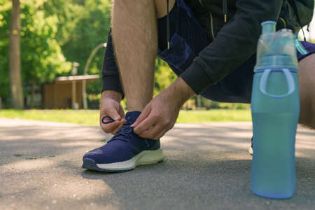 Young athletic man tying running shoes in the park outdoor, male runner ready for jogging on the...