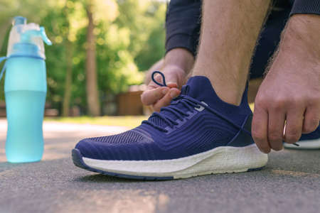 Man tying running shoes in the park at morning, male runner jogging on the road outside