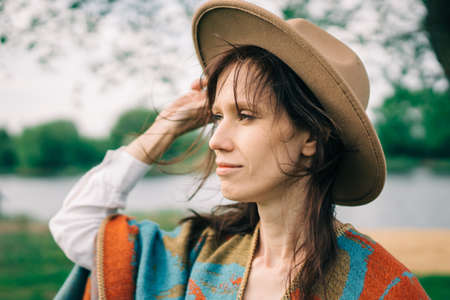 Portrait of a woman in a hat and poncho on countryside with river.
