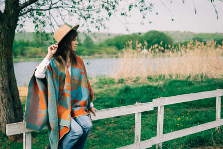 Woman sit on wooden fence on ranch and enjoying field view in farm in cloudy weatherの写真素材