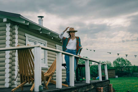 Woman in a hat and poncho, standing on porch of ranch american houseの写真素材
