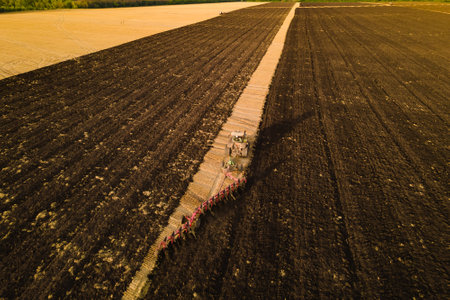 Tractor with harrow system plowing ground on cultivated farm field