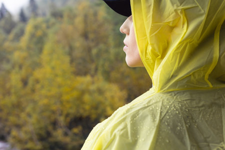 Rear view woman hiker in yellow raincoat hide from rain in forest, failed trekking