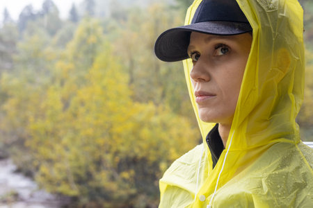Unhappy woman hiker in yellow raincoat hide from rain in forest, failed trekking