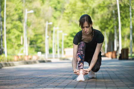 Young modern woman tying running shoes in urban park. full shot