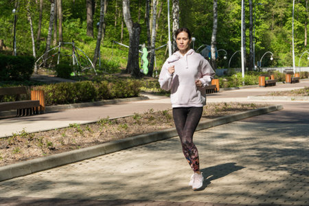 Young fitness woman running at morning city park, full shotの写真素材