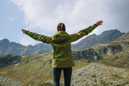 Hiker woman with raised arms on a mountain cliff at evening, back view