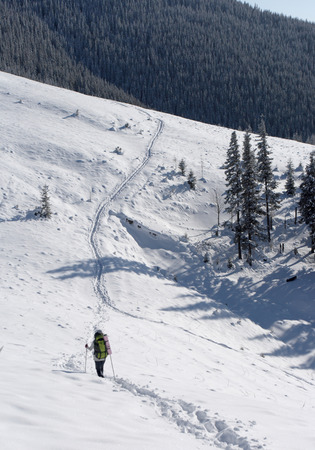 backpacker moving up in winter mountain under blue sky の写真素材