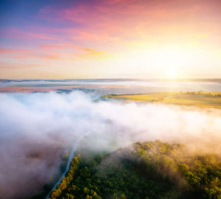 Awesome misty view of farmland and cultivated fields with a country road. Location place of Ukrainian agrarian region. Aerial photography, drone shot. Photo wallpaper. Discover the beauty of earth.の写真素材
