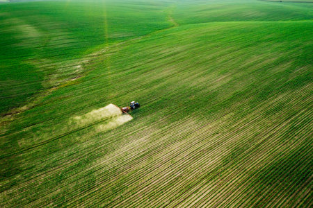Scenic top view of a tractor spraying green fields. Organic irrigation field. Location place of Ukraine agrarian region, Europe. Aerial photography, drone shot. Industry of agronomy. Beauty of earth.の写真素材
