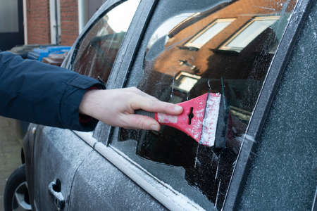 Cleaning the side car windows of snow with ice scraper before the trip. Man removes ice from car windows. A male hand.の写真素材