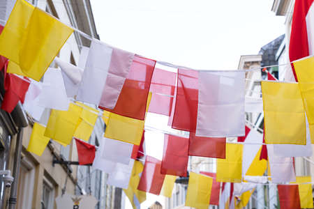 Many Dutch square flags on a ribbon, in red, white and yellow, or traditional festival named Carnaval, like Mardi Gras, in 's-Hertogenbosch, Oeteldonk with a blue skyの写真素材