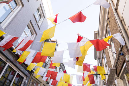 Many Dutch square flags on a ribbon, in red, white and yellow, or traditional festival named Carnaval, like Mardi Gras, in 's-Hertogenbosch, Oeteldonk with a blue skyの写真素材
