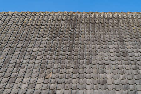 Roof with gray roof tiles and a clear blue sky with some clouds on a sunny dayの写真素材